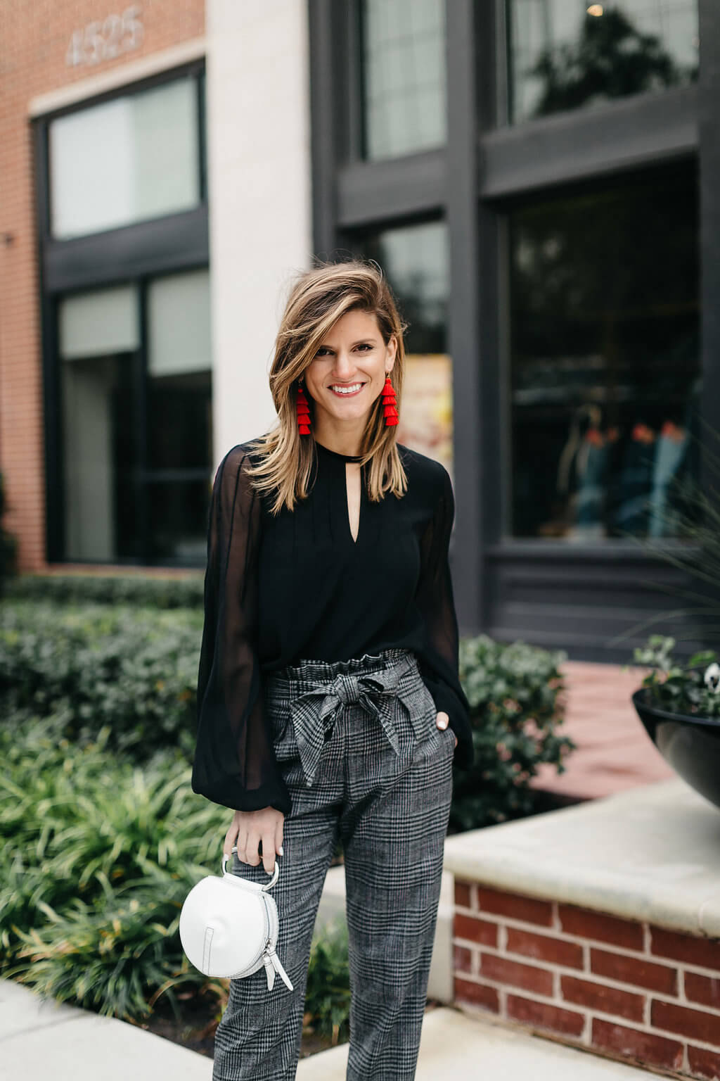 plaid trouser, black blouse, black pumps, and red tassel earrings 